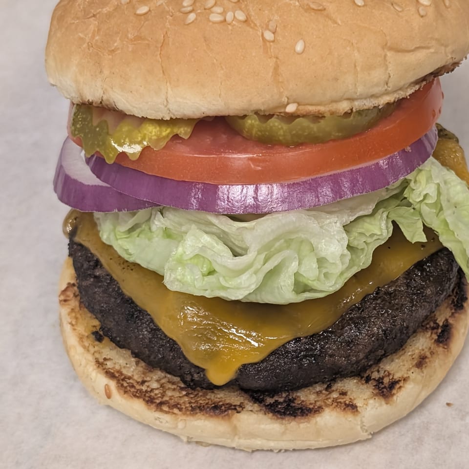 A Cap Hill burger with a sesame seed bun, cheese, lettuce, red onion, tomato, and pickles.