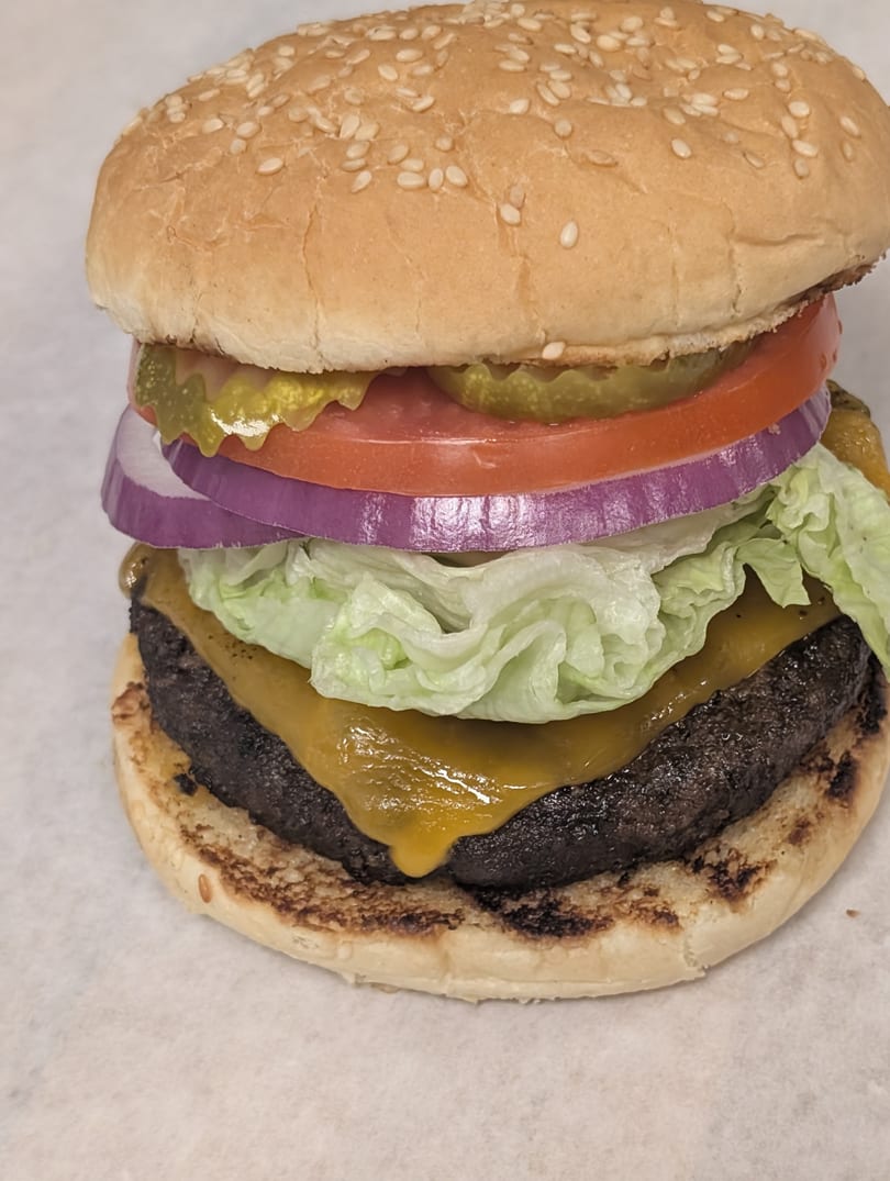 A Cap Hill burger with a sesame seed bun, cheese, lettuce, red onion, tomato, and pickles.